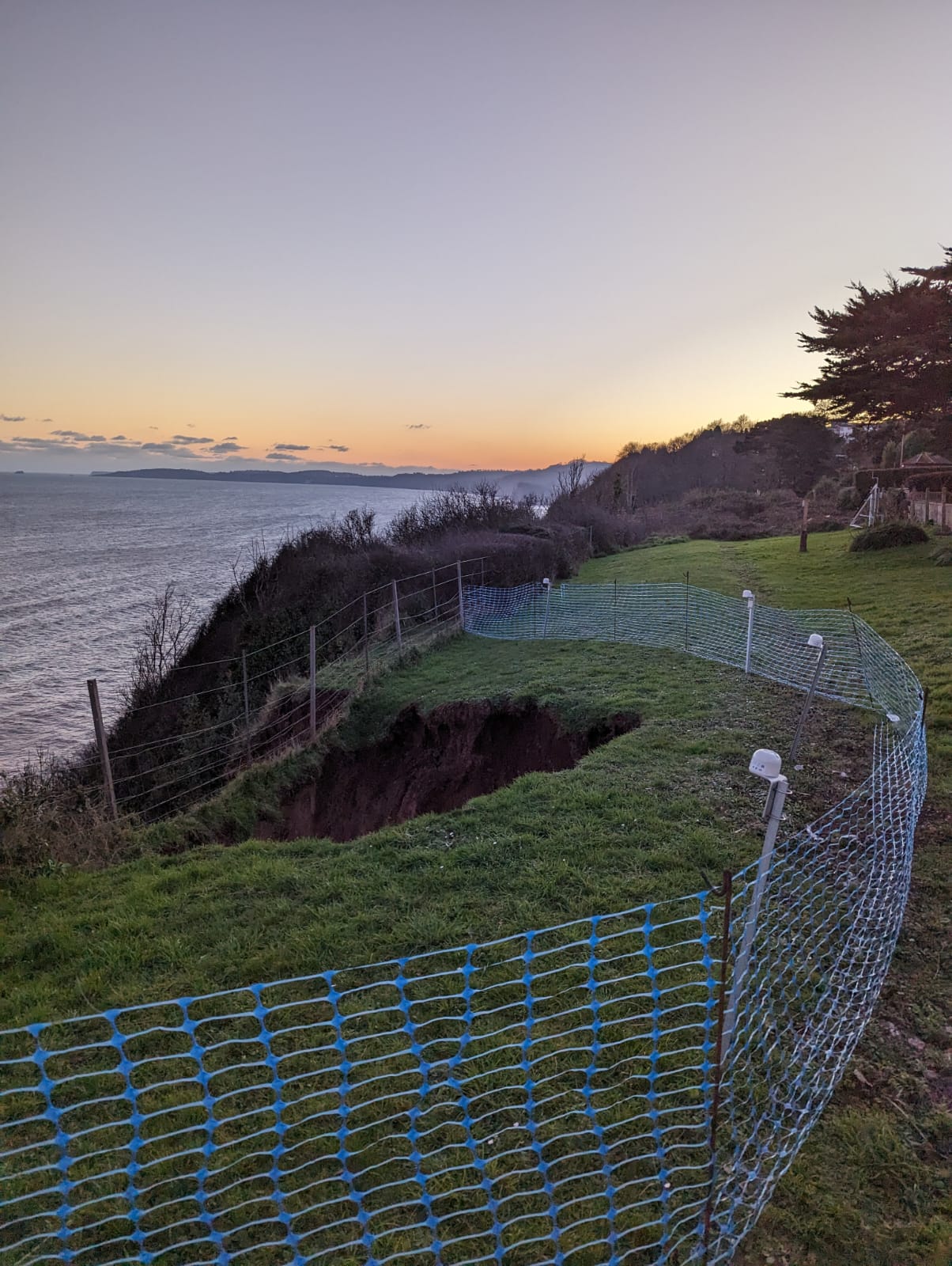 Image taken from the top of the cliff, showing the hole left by the slip and a series of tilt meters, which are enclosed by fencing, to monitor for further slips.