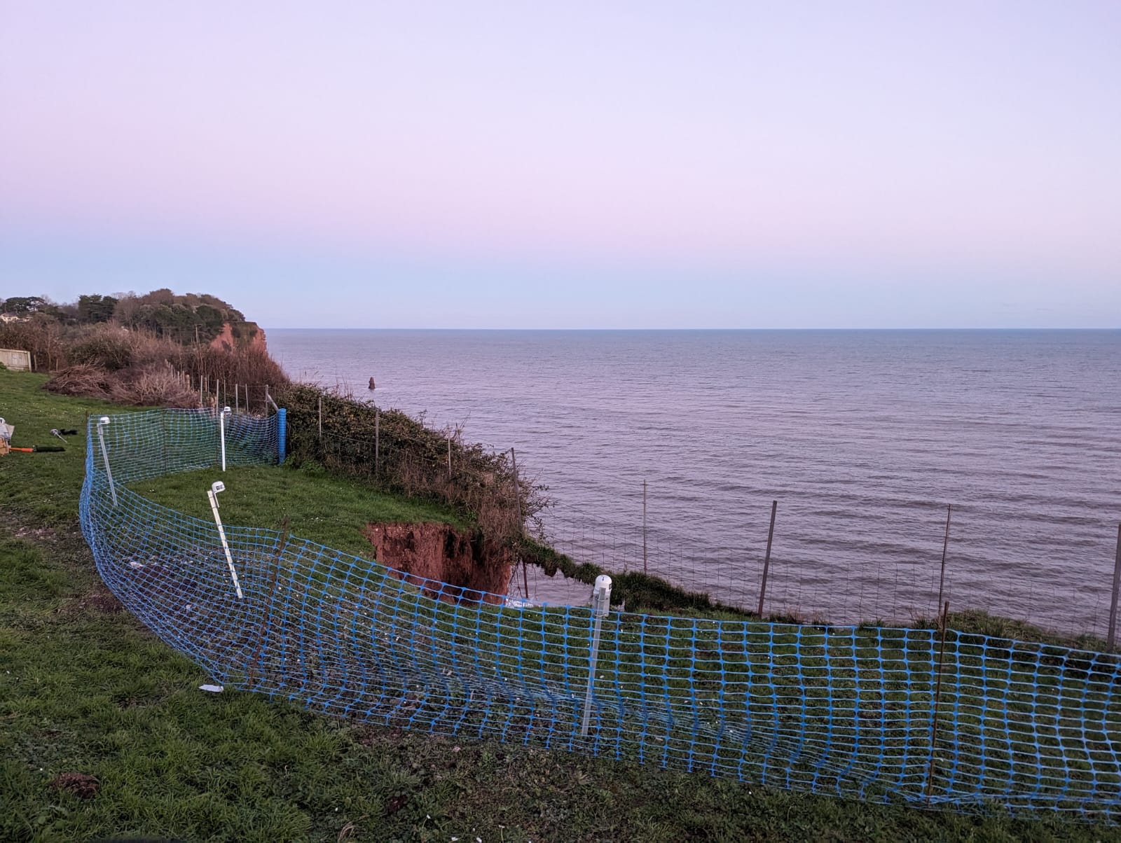 Image taken from the top of the cliff, showing the hole left by the slip and a series of tilt meters, which are enclosed by fencing, to monitor for further slips.